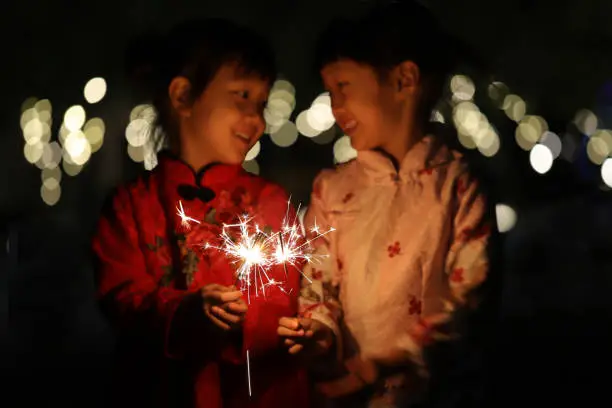 Photo of two smiling Asian girls playing sparkler and wearing cheongsam in Chinese New Year