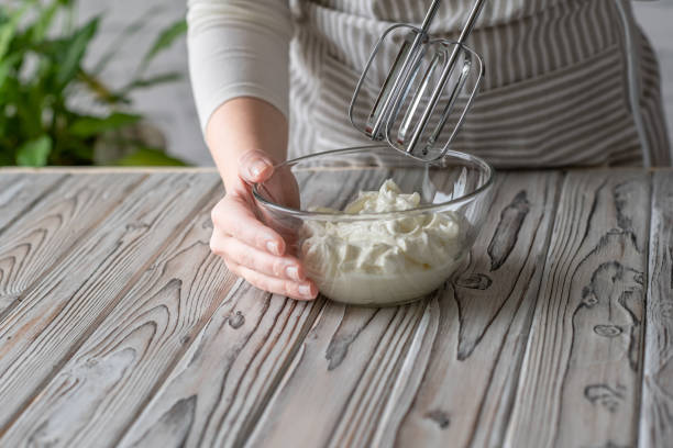 Woman whipping cream using electric hand mixer on the gray rustic wooden table Woman whipping cream using electric hand mixer on the gray rustic wooden table electric whisk stock pictures, royalty-free photos & images