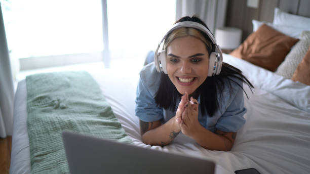 transgender woman watching something on laptop (or on a video call) at home - lying down women laptop freedom imagens e fotografias de stock