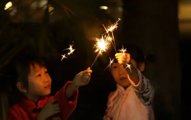 Photo of two smiling Asian girls playing sparkler and wearing cheongsam in Chinese New Year