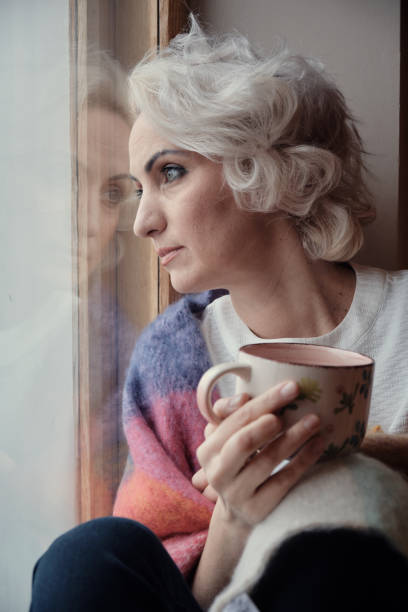 istock Sad pensive mature woman drinking tea and looking out window, lockdown and isolation concept, selective focus 1299629429
