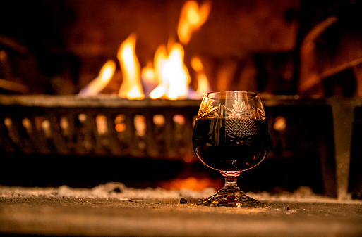 Brandy in crystal Glass by the burning fireplace. Relaxing in the evening with good drink