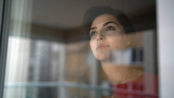 istock Young woman looking through window 1299630624