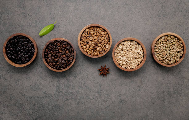 granos de café verdes y marrones sin tostar y tostados oscuros en un tazón de madera con cucharas sobre fondo de hormigón oscuro. - menu bean brown caffeine fotografías e imágenes de stock