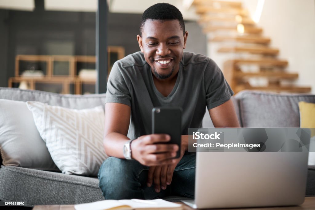 Just got that confirmation text Shot of a young man using a cellphone and laptop at home Men Stock Photo