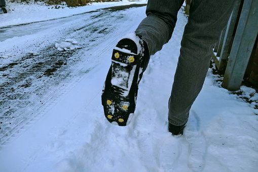 La suela de la bota negra de una persona que levanta su pierna izquierda está provista de protección antideslizante y picos. Equipo de seguridad para zapatos en invierno en hielo negro y nieve. photo
