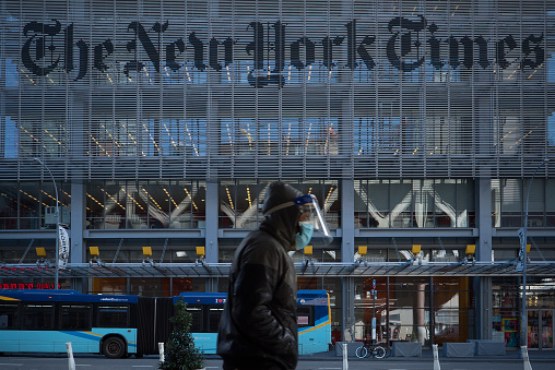 Manhattan, New York. January 28, 2021. A man wearing a mask and a face shield walks in front of the New York Times building in Midtown.