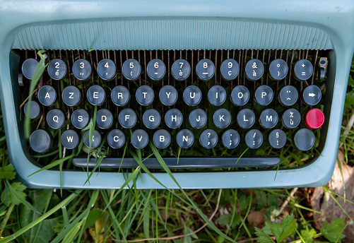 Old vintage blue typewriter on the green garden grass, top view