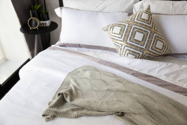 istock Comfortable bed with soft pillows, bed sheet, knitting blanket. Decorated with matal loft table, clock, small plants and beutiful design of lamp. 1299634922