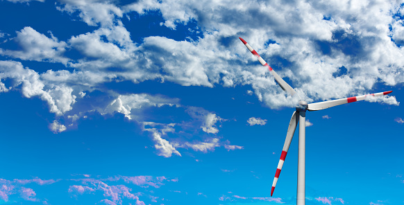 Wind turbine banner background\nTop view of wind turbine shrouded by clouds on blue sky background. Renewable energy banner concept.