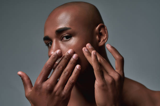 Close up shot of handsome young african american guy squeezing out a pimple on the cheek, posing isolated over grey background Close up shot of handsome young african american guy squeezing out a pimple on the cheek, posing isolated over grey background. Skincare concept. Horizontal shot skincare for men black stock pictures, royalty-free photos & images