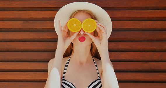 Summer portrait of woman covering her eyes with slices of orange wearing a straw hat on a background