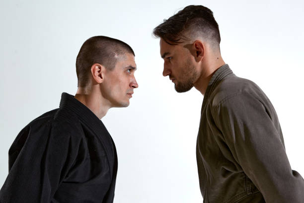 istock Guys in kimono standing in stance face to face before karate fight workout on white studio backdrop, close up portrait 1299645116