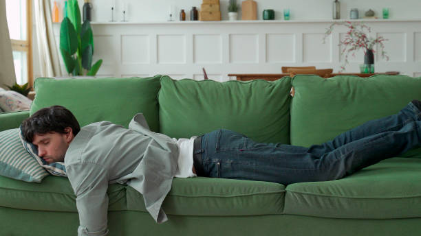 exhausted young man came home after work flopped down on sofa - exaustão imagens e fotografias de stock