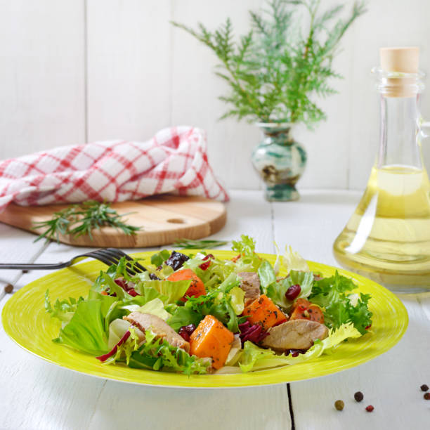 Dietary salad with roast turkey, pumpkin and green lettuce on a white wooden background.