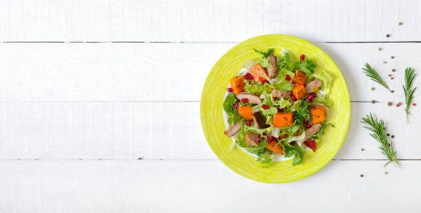 Dietary salad with roast turkey, pumpkin and green lettuce on a white wooden background. Top view. Copy space