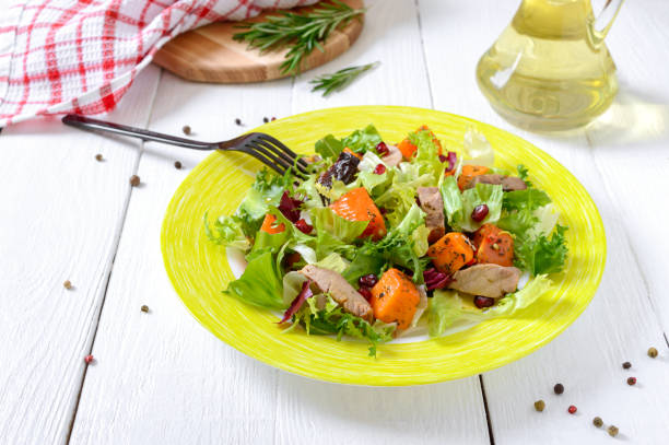 Dietary salad with roast turkey, pumpkin and green lettuce on a white wooden background.