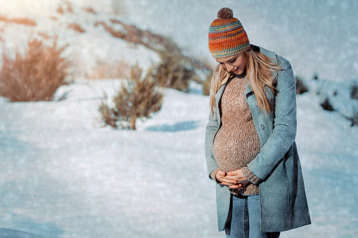 Nice Pregnant Woman Walking in the Countryside in Winter. Looking on the Tummy and Talking to the Baby. Happy Healthy Pregnancy.