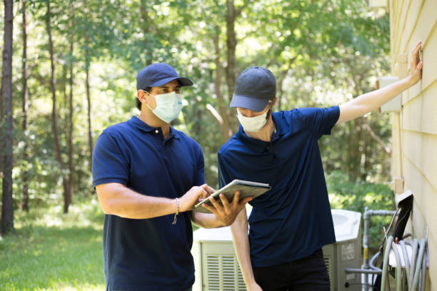 Inspector or blue collar workers examine building walls.  Outdoors. Repairmen, building inspectors, exterminators, engineers, insurance adjusters, or other blue collar workers examine a building/home's exterior walls.  One holds a digital tablet, and they both wear protective face masks due to CoVID-19. exterminator photos stock pictures, royalty-free photos & images