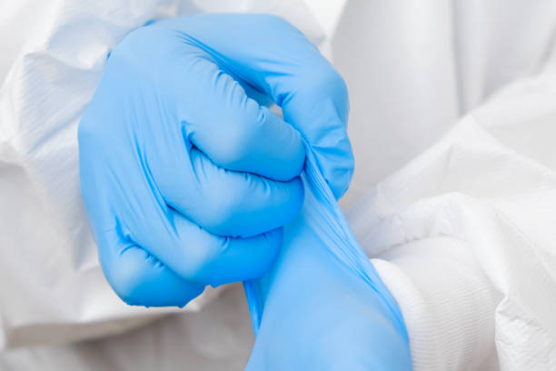 Doctor or nurse in protective PPE suit putting on rubber blue gloves before work with coronavirus patient or test samples or vaccination Doctor or nurse in protective PPE suit putting on rubber blue gloves before work with coronavirus patient, test samples or vaccination. putting on latex gloves stock pictures, royalty-free photos & images