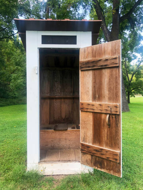 Colonial American outhouse with open door. Outhouse at the Hopewell Furnace National Historic site. Open door reveals interior. Green grass nature background. Outhouse stock pictures, royalty-free photos & images