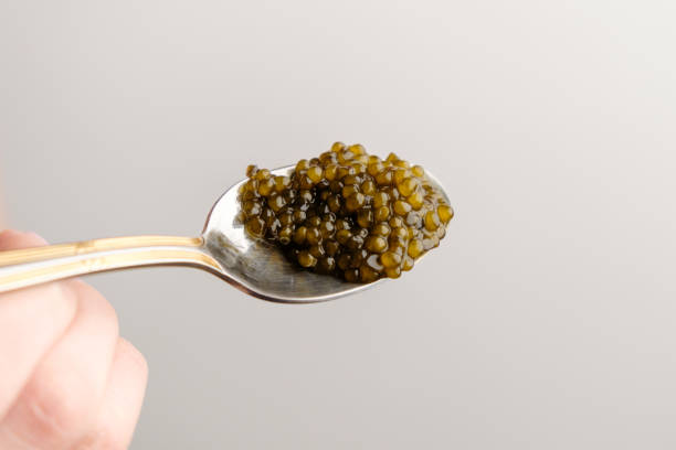 istock Black sturgeon caviar in a golden spoon on the white background with copy space. 1299658909