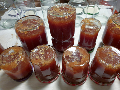 Sterilized glass jars filled with homemade quince jam are upside down on a wet cloth on the kitchen counter