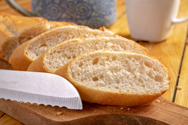 tasty and fresh baguette cut into pieces. bread and a chopping knife in the home kitchen. light background. - buns of steel imagens e fotografias de stock