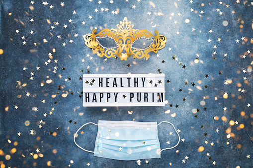 Healthy Happy Purim written in lightbox and two masks on a blue background. Purim Carnival celebration concept.