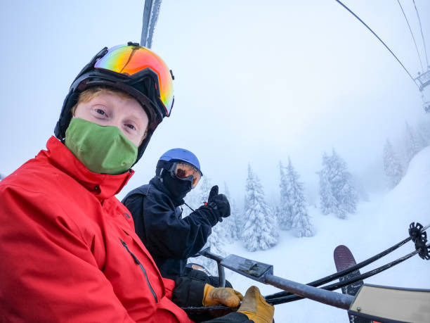 Two Men Wearing Face Mask and Neck Gaiter on Chairlift Son and father on chairlift wearing face mask and neck gaiter. Face coverings required for skiing in North Vancouver, British Columbia, Canada. thumbs up for skiing stock pictures, royalty-free photos & images