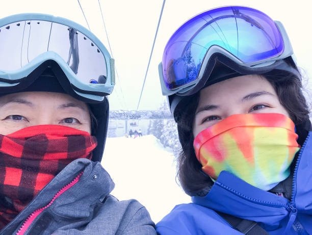 asian mother, eurasian daughter wearing neck gaiters riding ski lift - mt seymour provincial park imagens e fotografias de stock