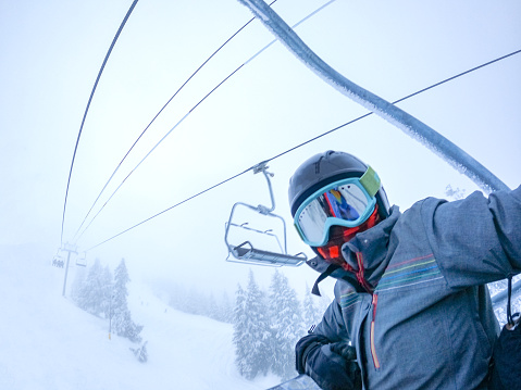 Woman snowboarder on chairlift wearing neck gaiter.  Face coverings required for skiing and snowboarding in North Vancouver, British Columbia, Canada.
