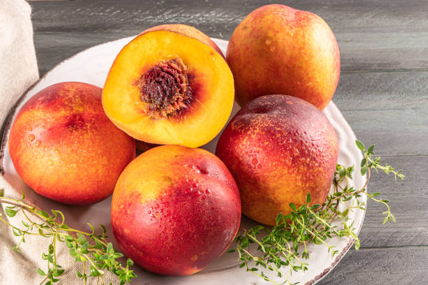 istock Ripe peaches with thyme leaves in a plate on a wooden board on a background 1299668497