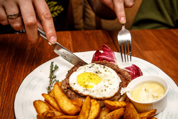 istock Close-up of hands that cut the beefsteak with scrambled eggs and fried potatoes on the white plate. Side view. 1299671737