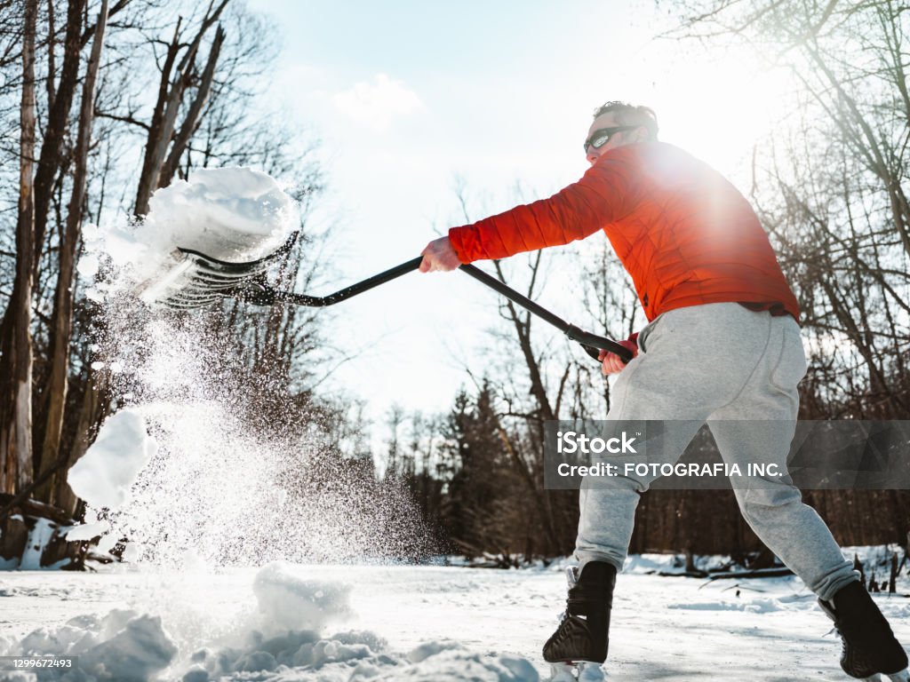 Mature man clearing snow Mature man clearing up snow on outdoor ice skating rink. Exterior of frozen pond in public park. Snow Stock Photo