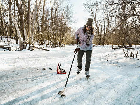 Mature woman playing hockey outdoors. Exterior of frozen pond in public park.