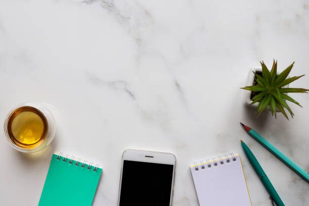 istock Modern office table desk with copy space. Workspace with notepads, pen, smartphone, cup of tea and succulent plant on light gray marble background. Workspace organization. Top view, flat lay 1299673583