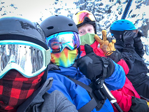 Selfie of family group on chairlift wearing neck gaiters and face mask.  Face coverings required for skiing in North Vancouver, British Columbia, Canada.