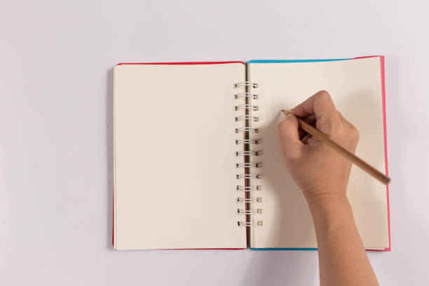 istock Hand woman writing on Blank Notebook isolated on the white background. office concept top view 1299676427
