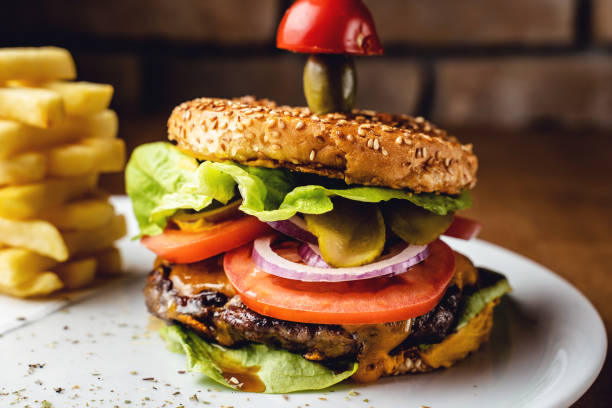 istock Burger with beef tomato onion and lettuce leaves on a plate with brick wall background - Burger with potato chips served at restaurant 1299678190
