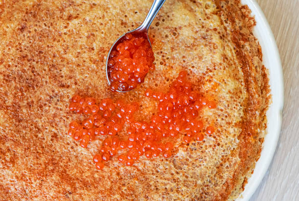istock Pancakes with red caviar on a plate. Next to pancakes is a spoon with caviar. Light background. Close-up. 1299679190