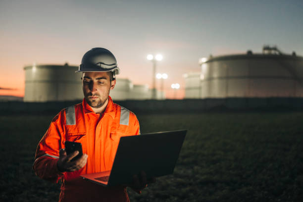 istock Engineer using laptop near oil refinery at night 1299679449