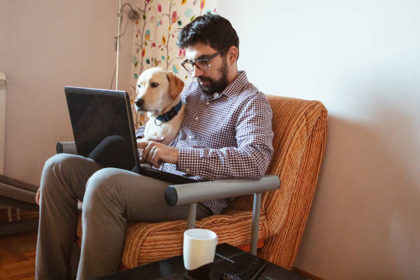 istock Man working on laptop at home, his pet dog is next to him 1299679781