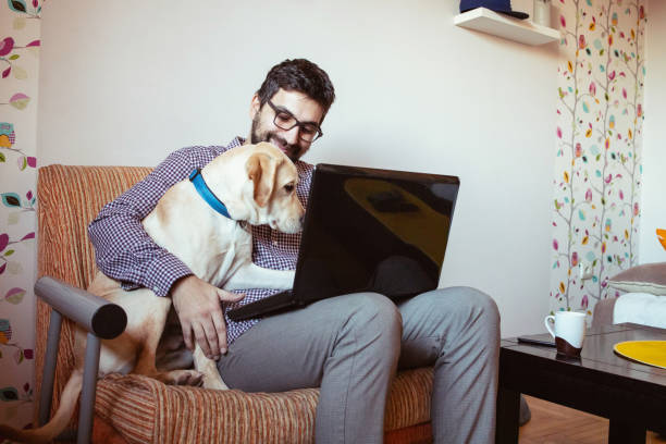 istock Man working on laptop at home, his pet dog is next to him 1299680048