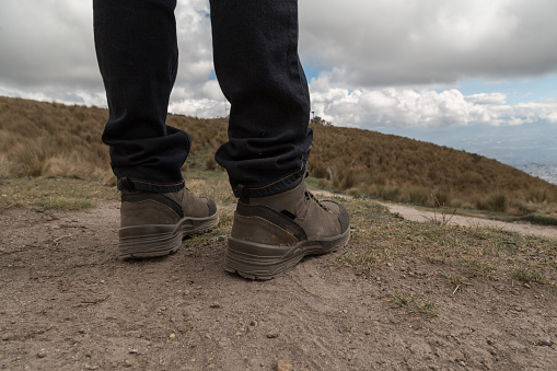 man in jeans and boots on a hike on a mountain with a landscape with a gray sky and clouds