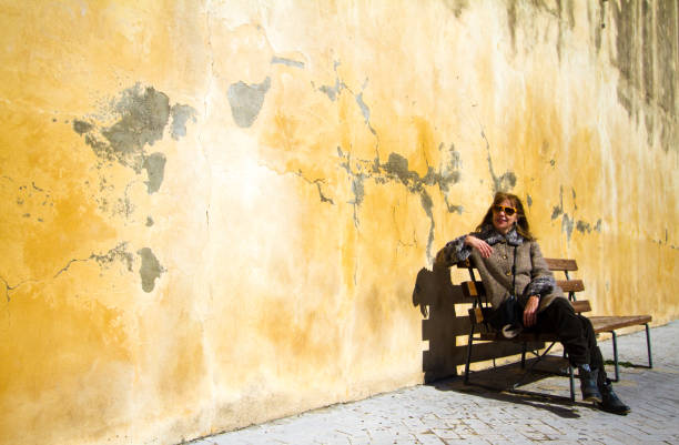 istock Woman Sitting Near Old Weathered Yellow Wall 1299687087