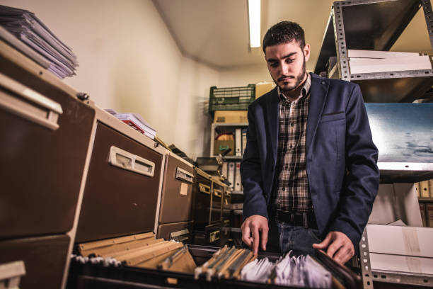 istock Man in dark file basement works in office searching old documentation file. 1299688402