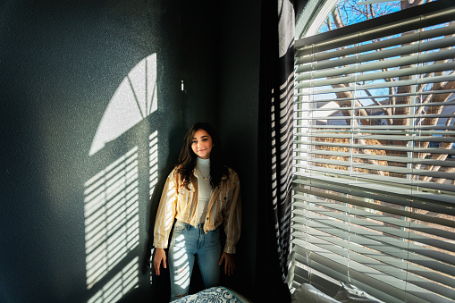 Dramatic Window Lit Portrait of a Beautiful Hispanic Woman in her Twenties against a Grey wall with shadows