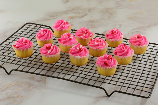 Pink Valentine's Day cupcakes with tiny candy hearts sitting on cooling rack after final decorating completed