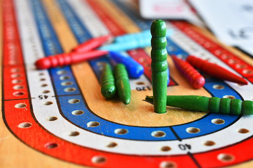 A close up image of a green cribbage pegs in the winning position on a cribbage board.